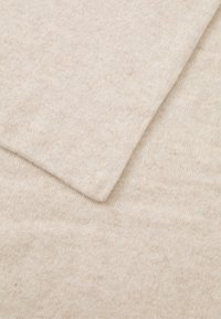 Primo piano di un morbido tessuto lavorato a maglia beige con un bordo piegato che mostra la fine texture della lana e i dettagli delle cuciture.