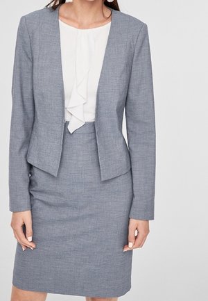 Blazer gris avec une coupe ajustée et une légère brillance, associé à un chemisier blanc à col volanté et à une jupe crayon ajustée.