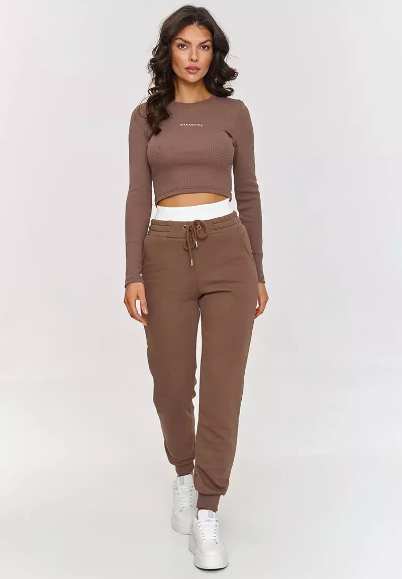 Brązowy prążkowany długi rękaw crop top z logo, w połączeniu z dopasowanymi dresami z elastycznym paskiem w talii i ściągaczami przy kostkach oraz białymi sneakersami.