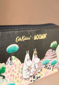 Juodas Moomin spaudinio piniginė su užtrauktuku, puošta gėlių raštais, dviem Moomin personažais ir žaliomis medžio detalėmis. Viršuje auksinis logotipo užrašas.