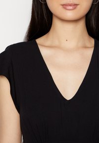 Vestido preto com decote em V, mangas curtas e detalhes franzidos na cintura. Textura suave e lisa.