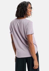 Camiseta de manga corta en lila, de tejido suave, con un corte relajado y puños enrollados. La parte de atrás presenta un dobladillo redondeado.
