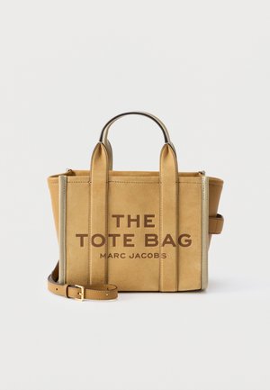 Beżowa torba typu tote zamszowa z podwójnymi uchwytami, odpinanym paskiem oraz nadrukiem "THE TOTE BAG MARC JACOBS" z przodu.