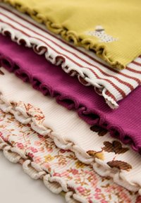 Montón de piezas de tela de canalé plegadas con bordes fruncidos en mostaza, rayas blancas y marrones, morado, crema y patrones florales.
