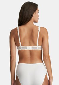 White lace-trimmed bra with adjustable straps, a hook-and-eye closure, and smooth fabric. High-waisted matching white underwear visible below.