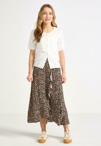 Cardigan bianco a maniche corte con bottoni, abbinato a una gonna a stampa leopardata marrone con orlo arricciato e sneaker chiare.