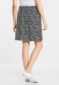 Černobílá sukně se geometrickým vzorem, ve tvaru A, délka ke kolenům, hladká látka, v kombinaci s bílými teniskami.