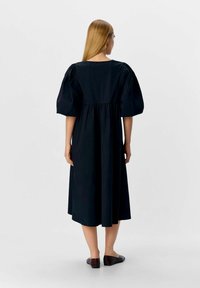 Robe noire midi avec des manches bouffantes, taille cintrée et jupe plissée. Texture en coton lisse, design minimaliste et sans motifs visibles.