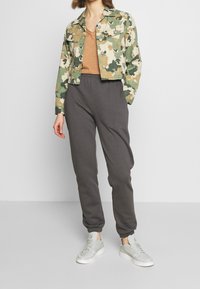 Kamikaze-mönstrad kort jacka, ljusbrun v-ringad topp, grå mjukisbyxor och grå sneakers. Jackan har knappar och två bröstfickor.