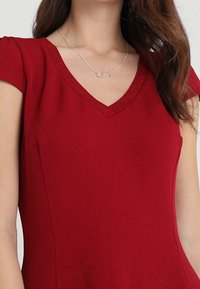 Top rojo de cuello en V con mangas cortas, textura suave y un ligero brillo en el escote. Diseño simple, silueta ajustada, sin patrones visibles.