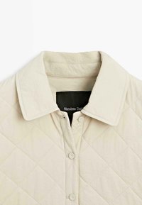 Béžová prošívaná bunda s špičatým límcem, zapínáním na knoflíky vpředu a hladkým povrchem s prošíváním ve tvaru diamantů.