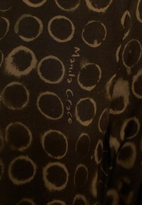 Tessuto marrone con un motivo circolare di dimensioni variabili. Il design include tonalità più chiare e più scure con l'etichetta "Manila Grace" visibile.