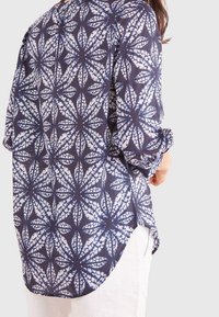 Camicia a maniche lunghe blu navy con un motivo floreale bianco, in tessuto leggero, con orlo curvo e maniche arrotolate.