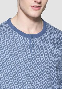 Camicia a maniche corte blu con motivo, dotata di colletto henley, due bottoni e un design geometrico a spina di pesce su un tessuto testurizzato.