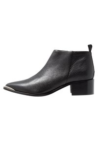 Schwarze Lederankelstiefel mit strukturierter Oberfläche, spitzer Zehenpartie und niedrigem Blockabsatz. Mit einem metallischen Akzent an der Zehenkappe.