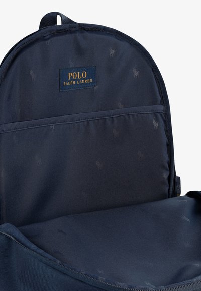 Notranjost mornarsko modre platnene nahrbtnika z logotipom, ki ima gladko teksturo in subtilen ponavljajoč vzorec polo igralca.