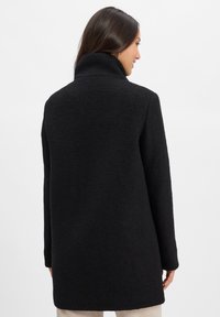 Black wool coat with a high collar, textured fabric, slightly oversized fit, and straight silhouette. Features no visible fasteners.