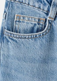 Tissu en denim bleu clair avec une poche cousue bien visible. La texture est légèrement délavée avec des détails de surpiqûres orange contrastantes.