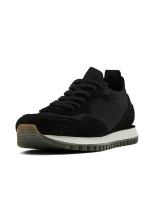 Zwarte sneaker met een mix van mesh en suede materialen, ronde neus, getextureerde zool en contrasterende witte tussenzool. De veters zijn duidelijk zichtbaar.