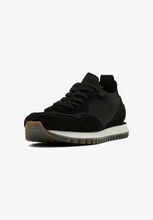 Sort sneaker med en blanding af mesh og ruskindsmaterialer, rund tå, tekstureret sål og kontrasterende hvid mellemsål. Snørebåndene er tydeligt vist.