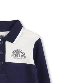 Marineblauwe en witte polo met een knoopsluiting. Bevat het logo "Timberland EST 1973" in donkerblauw. Zachte katoenen blend textuur.