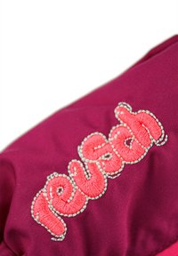 Lila Stoff mit gesticktem "reusch" in leuchtendem Pink; detaillierte Stickerei in Weiß. Das Design weist eine glatte, strukturierte Oberfläche auf.