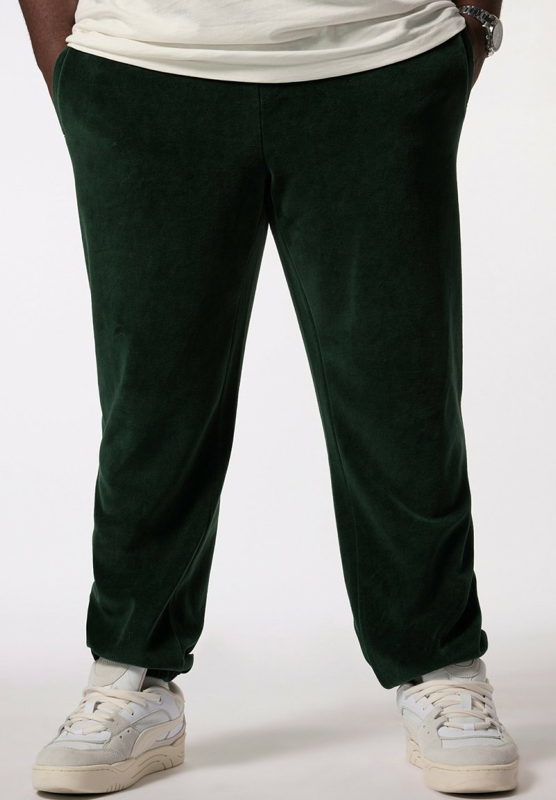 Gröna sammetsträningsbyxor med avslappnad passform, med en mjuk textur och subtil lyster, tillsammans med ljusfärgade sneakers.