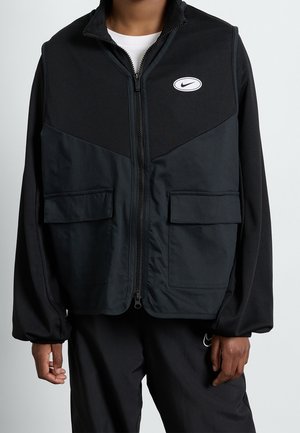 Sort lynlåsvest med mesh øverst, to forlommer og en lille hvid Nike-logo. Glat tekstur med en afslappet pasform og elastiske manchetter.