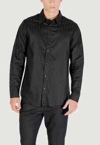 Camicia nera a maniche lunghe con un motivo a diamante testurizzato, apertura frontale con bottoni e bottoni neri. Indossata con pantaloni neri.
