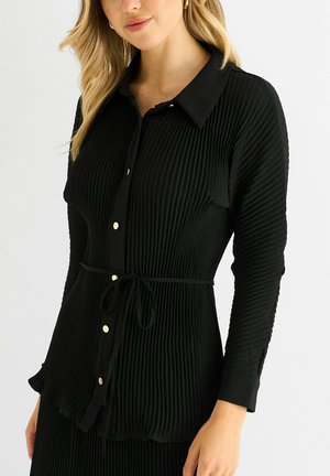 Black pleated blouse with a collar, button front, and tie waist. Features gold buttons and long sleeves with textured fabric.