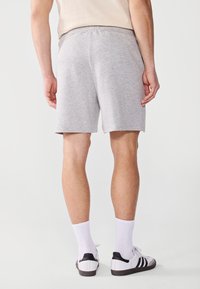 Shorts en coton gris avec une taille élastique, longueur mi-cuisse, associés à des chaussettes blanches et des baskets avec des accents noirs.