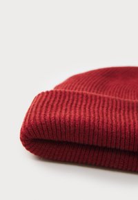 Red knitted beanie with a ribbed texture, featuring a folded cuff and soft fabric. The design is simple and functional.