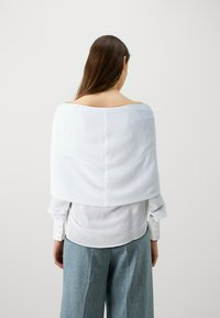 Hvit, gjennomsiktig stoffbluse med off-the-shoulder design; lange ermer med knappedetaljer; kombinert med lyseblå, vide bukser.