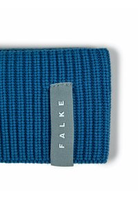 Tessuto a maglia blu con un'etichetta grigia cucita sopra, che mostra la parola "FALKE" in lettere maiuscole bianche.