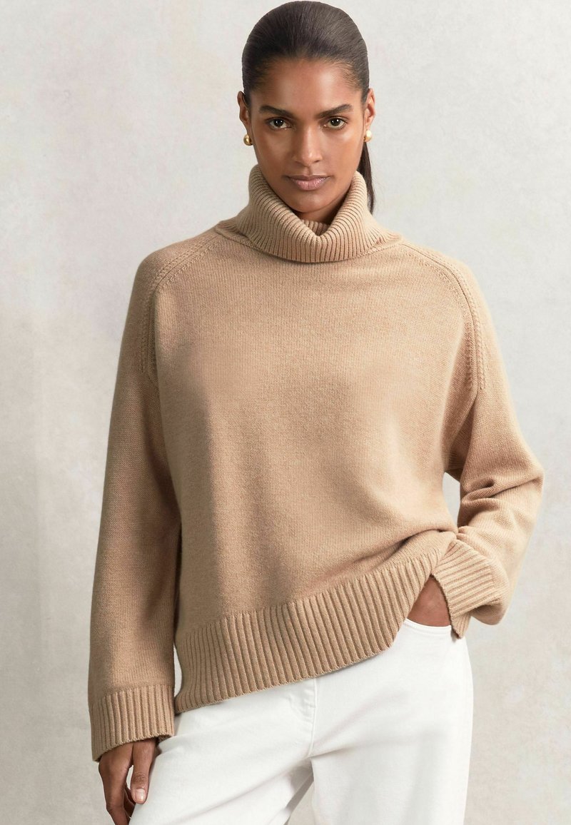 Beige coltrui gemaakt van zacht materiaal, met een ribbelboord aan de onderkant en mouwen, met een relaxte pasvorm en zijsplitten.