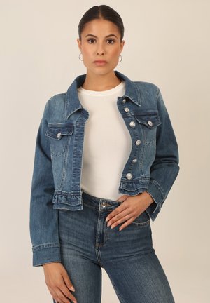 Denim jacket in medium wash, featuring a classic collar, button closure with metallic accents, and a cropped design. Paired with high-waisted jeans.