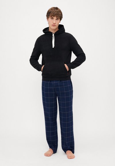 Μαύρη φόρμα με κουκούλα, διαθέτει μπροστινή τσέπη και λευκά κορδόνια, συνδυασμένη με ναυτική καρώ πιτζάμες που έχουν σχέδιο πλέγματος και μαλακή υφή.