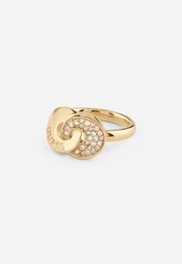 Gold-tone ring featuring a knot design with a textured surface and embedded clear rhinestones on one side, branded with "Guess."