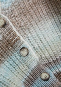Sweter z dzianiny z gradientem jasnoniebieskich i brązowych odcieni, z czterema dużymi, okrągłymi, kremowymi guzikami na fakturowanej tkaninie.