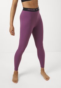 Lila leggings rugalmas anyagból, magas derékkal, fekete és rózsaszín "Venum" logóval. Sima felület és testhez álló kialakítás.