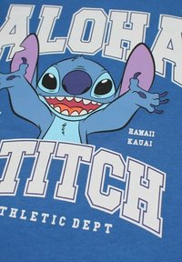 Personnage de dessin animé bleu Stitch les bras ouverts en souriant, grand texte "ALOHA STITCH" et texte plus petit "Hawaii Kauai Athletic Dept" sur fond bleu.