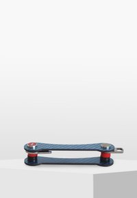 Multi-tool med ett blått kolfiberhölje, röda accenter och silverdetaljer. Har en hopfällbar design med ett korssymbol nära gångjärnet.