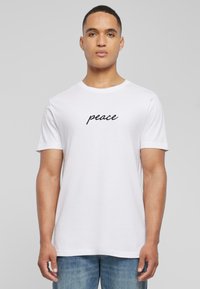 Hvid bomulds T-shirt med korte ærmer, der har ordet "fred" i sort kursiv skrift centreret på brystet.