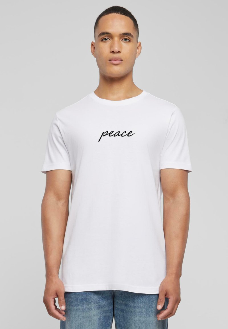 Hvid bomulds T-shirt med korte ærmer, der har ordet "fred" i sort kursiv skrift centreret på brystet.