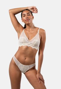 Lace-trimmed, sheer beige bralette en bijpassende string. Heeft delicate patronen en verstelbare bandjes. Zachte, lichte textuur.