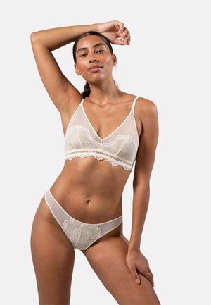 Lace-trimmed, sheer beige bralette en bijpassende string. Heeft delicate patronen en verstelbare bandjes. Zachte, lichte textuur.