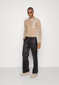 Beige long-sleeve shirt with a floral design on the left shoulder, paired with black leather pants and beige sneakers.