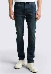 Ciemnoniebieskie dżinsy slim fit z pięcioma kieszeniami, zapięciem na guziki i subtelnymi detalami szycia. W połączeniu z białymi trampkami.