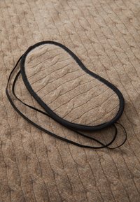 Black-bordered, oval-shaped wool insole placed on a textured, light brown cable-knit fabric. The insole features a soft, fuzzy surface.