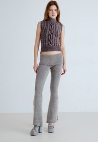 Maglione lavorato a maglia con collo alto e motivo a treccia, abbinato a pantaloni a maglia a righe con bottoni laterali e orli svasati, in colori neutri.